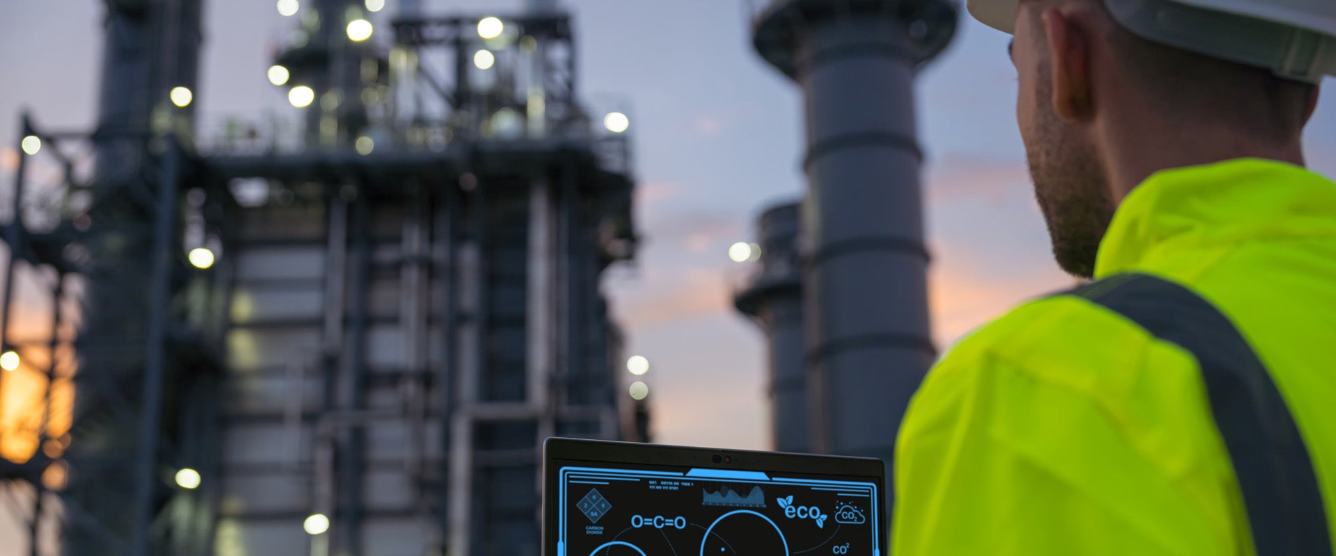 Man standing outside at an oil refinery with a laptop