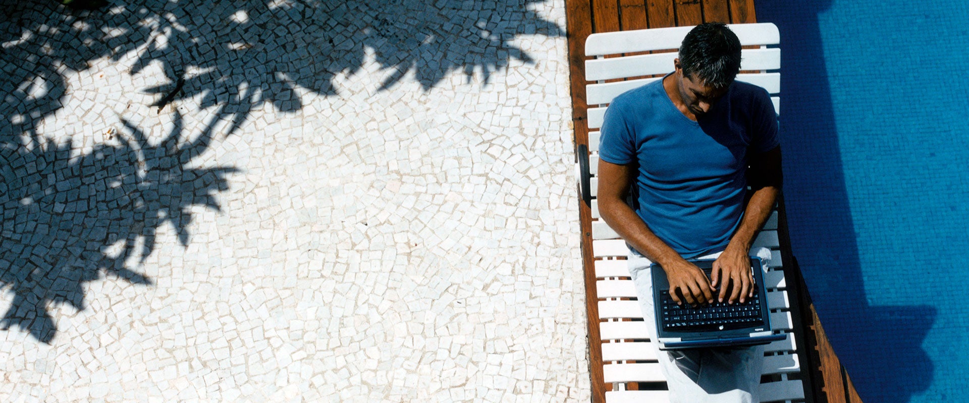 man lounging by pool with laptop