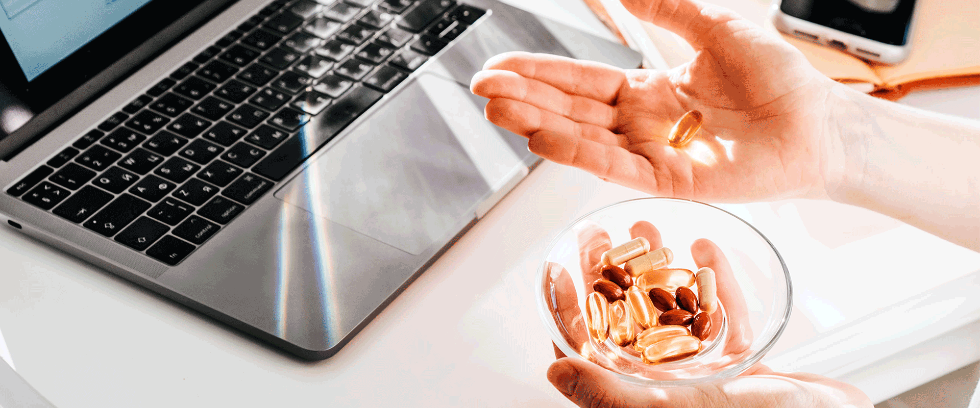 hands holding pills over a laptop