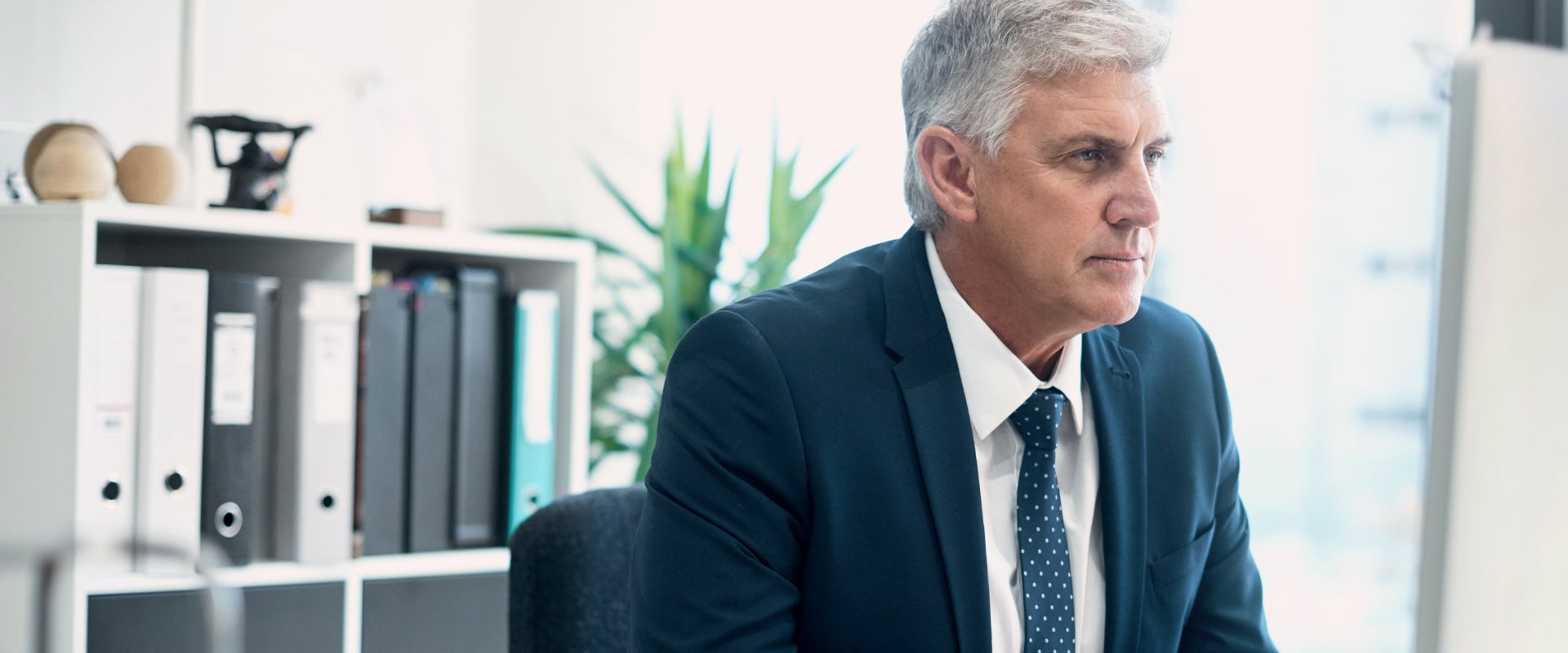 A person in a suit sitting at a desk in an office setting, focused on a computer screen. 
