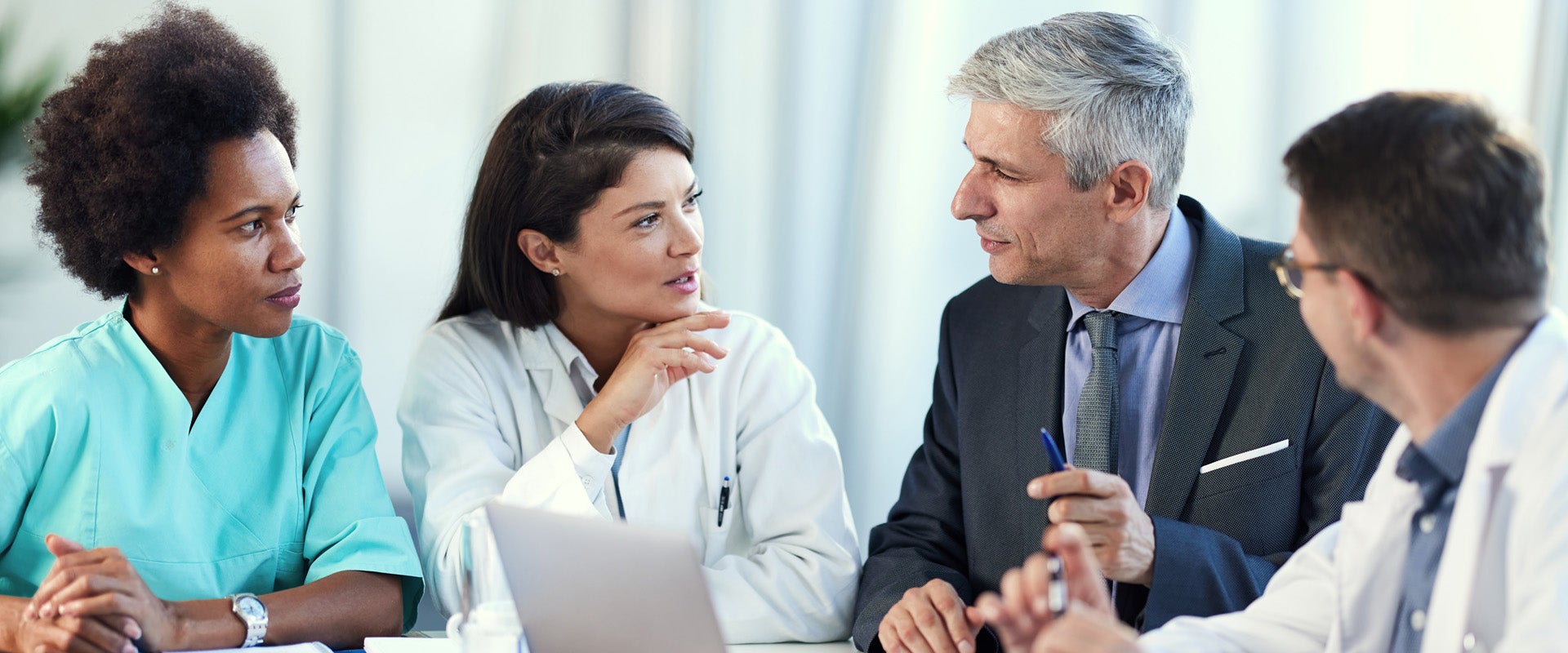 A group of medical professionals sitting around a laptop at a meeting table