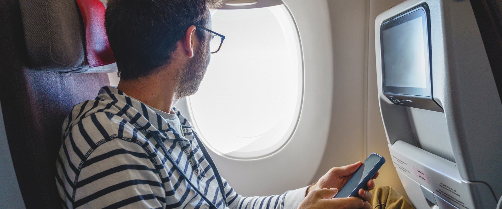 Man holding phone looking our window of plane